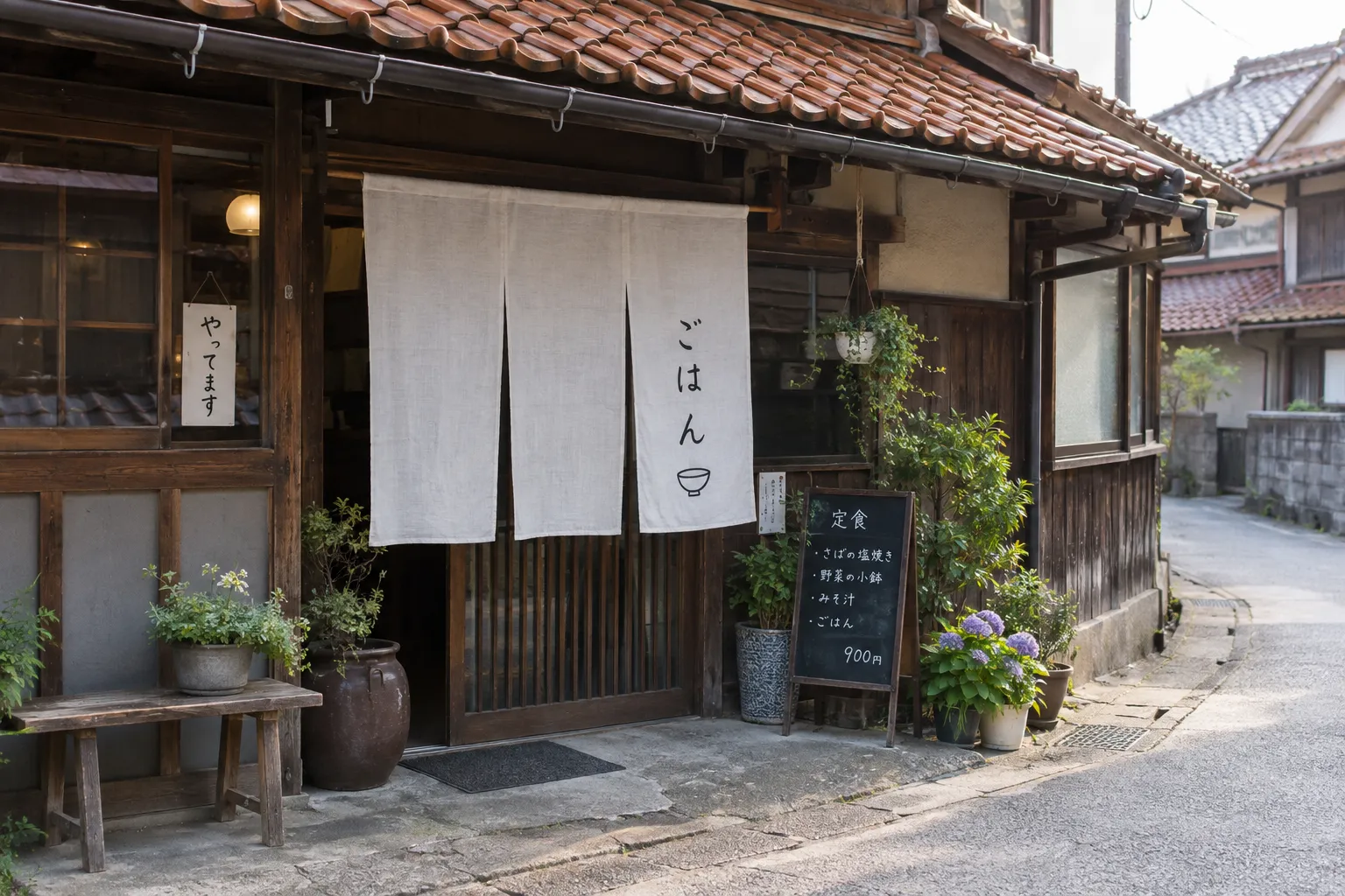 のれんと手書きの黒板を出した、赤い瓦屋根の小さなごはん屋の店先